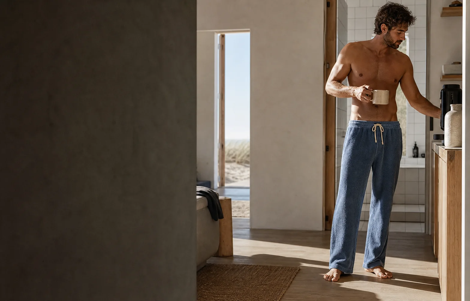 Man making coffee in faded blue Towel Trousers in a sunlit coastal home after showering